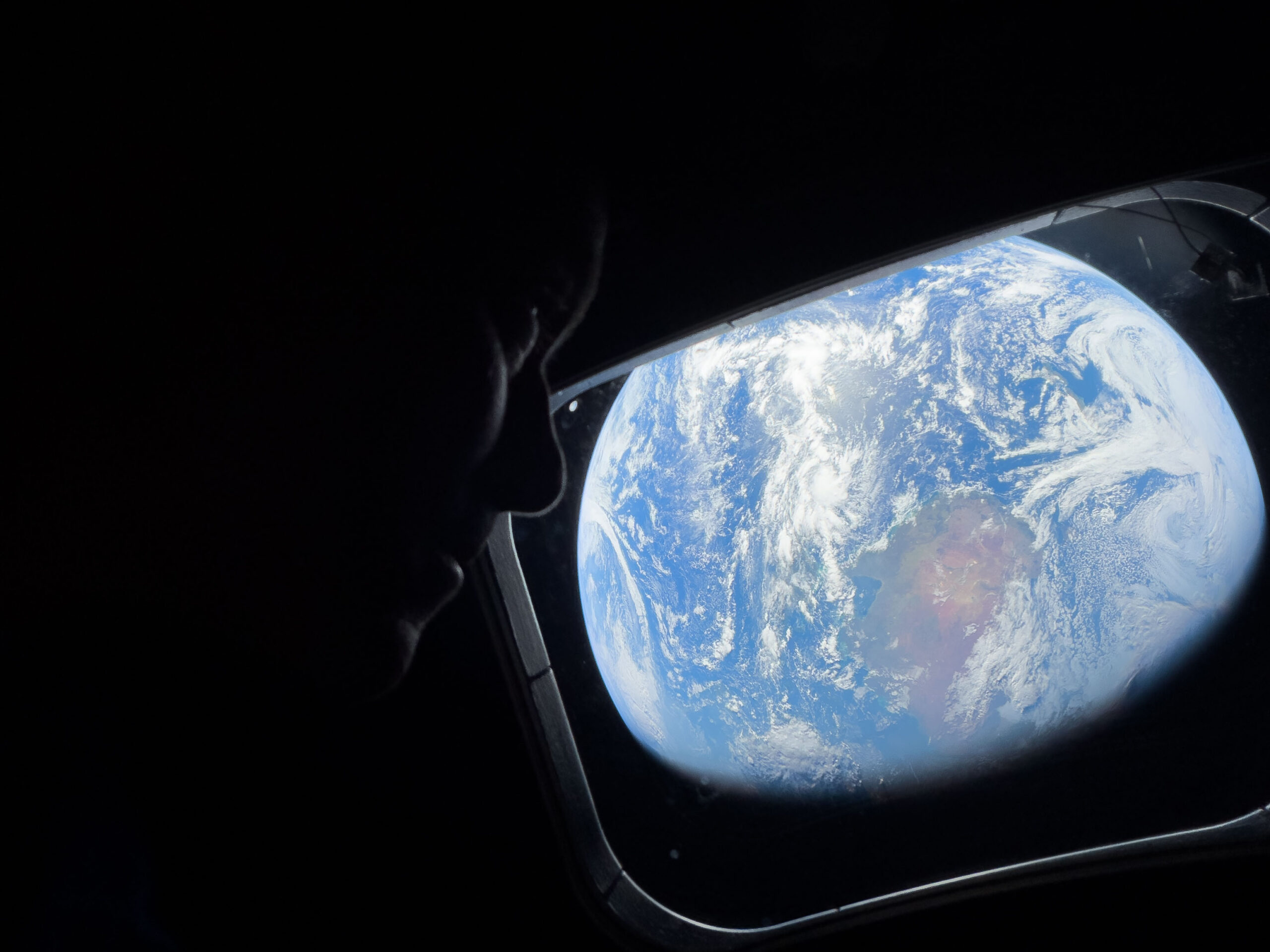 NASA astronaut and Artemis II Commander Reid Wiseman peers out of one of the Orion spacecraft's main cabin windows, looking back at Earth, as the crew travels towards the Moon.
