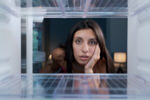 Photo of a dark haired woman looking into an empty fridge