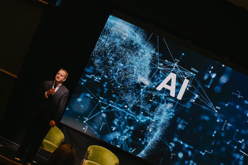 Photo of Pascal Fintoni talking about Responsible AI at NTBF Conference with the letters AI appearing behind him on a large screen