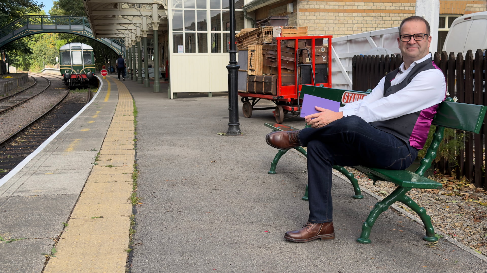 Photo of Pascal Fintoni sat on a bench at Stanhope Heritage Railway Station holding his field notebook
